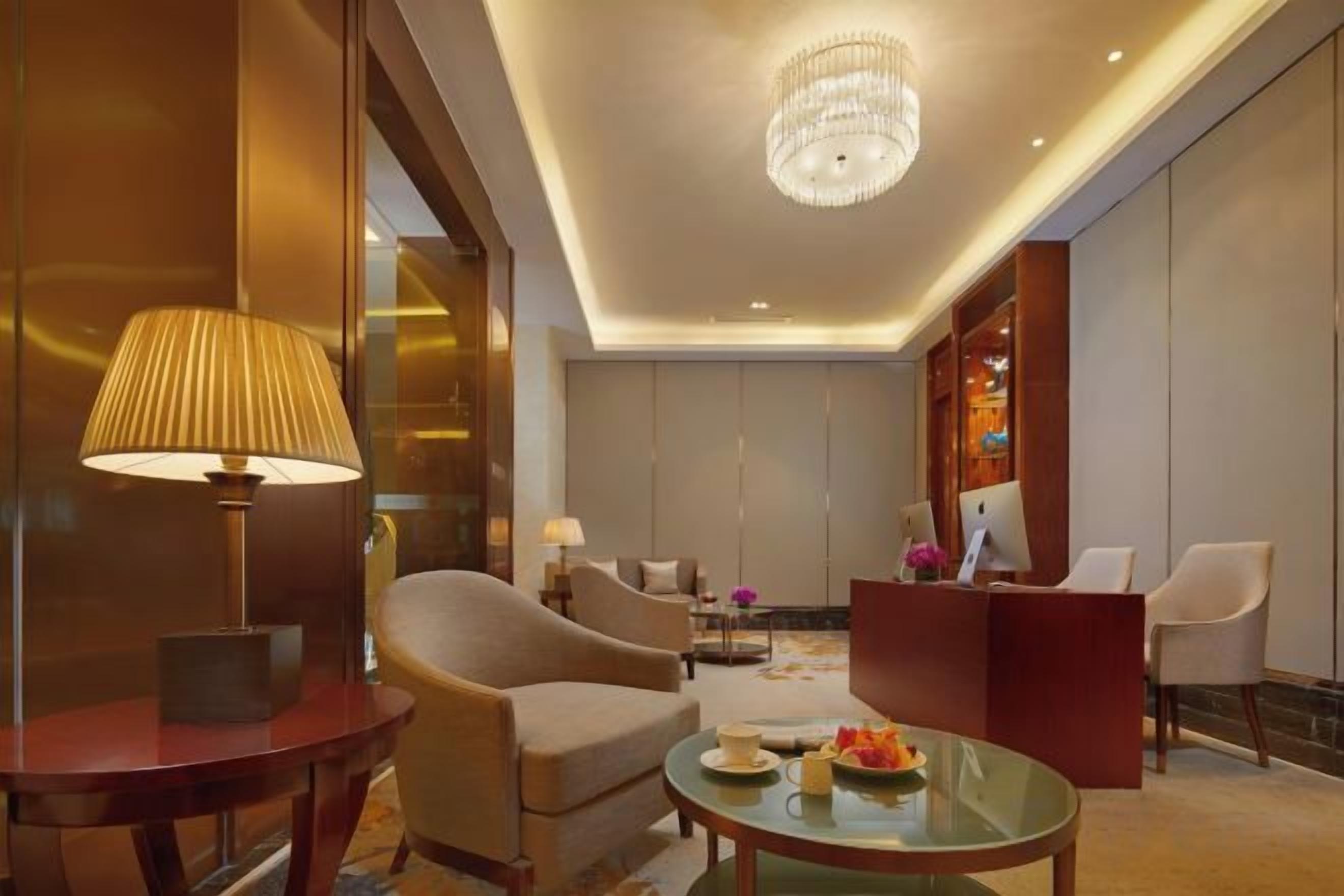 A hotel lobby with a reception desk, seating area, and a chandelier.