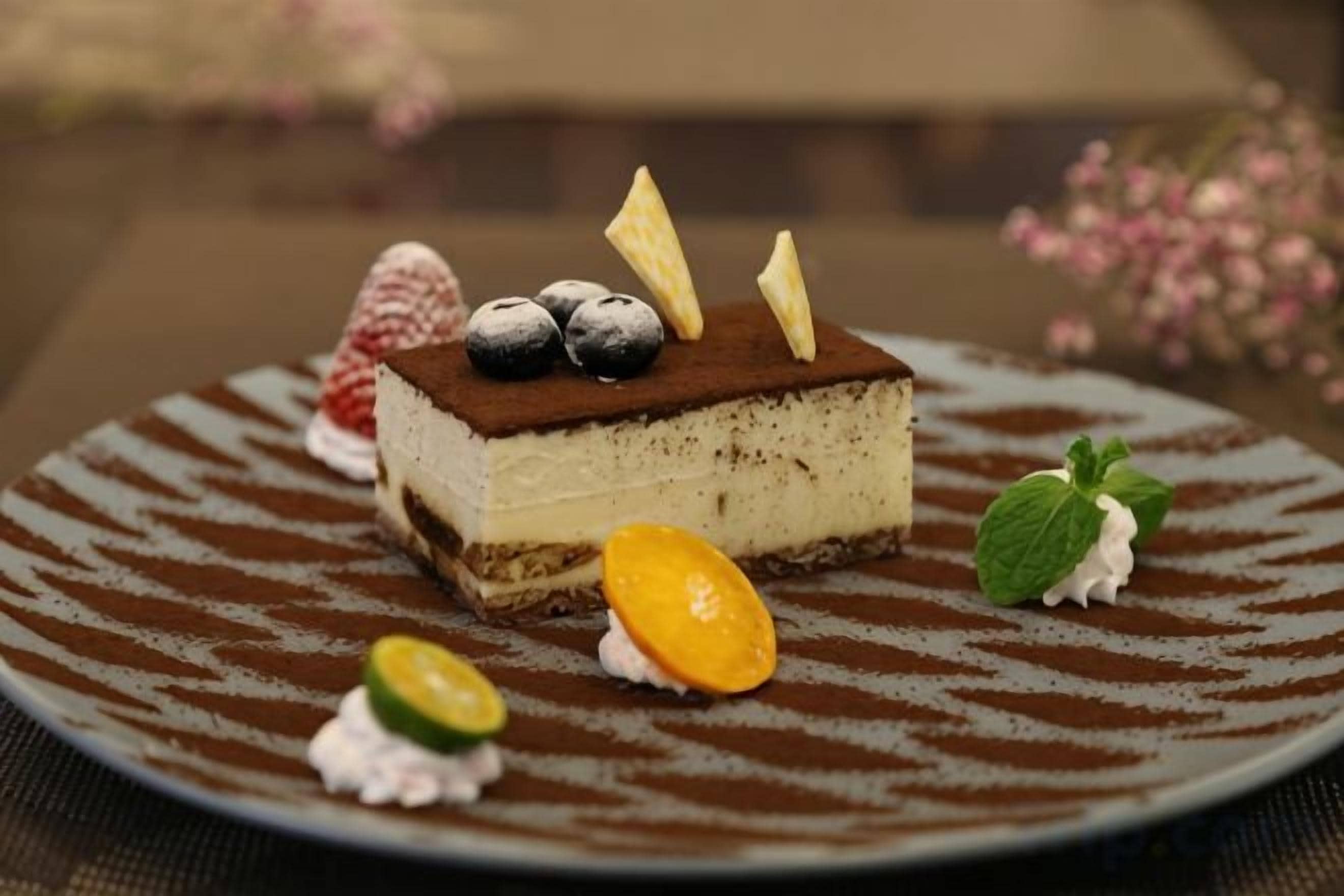 A dessert on a plate with a patterned design, accompanied by a mint leaf and a slice of fruit.