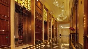 A hotel corridor with wooden paneling, a reflective floor, and a decorative ceiling light fixture. - Sanyu Grand New Century Hotel (Wenzhou)