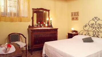 A bedroom with a bed, a wooden dresser, a chair, a nightstand, and a chandelier.