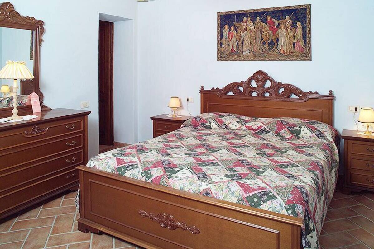 Ein Schlafzimmer mit einem hölzernen Bett, einem Schminktisch, einem Nachttisch, einem Spiegel und einem Gemälde an der Wand.