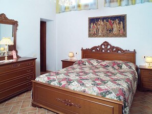 Un dormitorio con cama de madera, cómoda, mesita de noche, espejo y un cuadro en la pared.