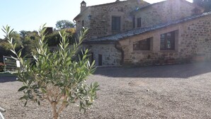 Un bâtiment en pierre avec une allée de gravier et un petit arbre au premier plan.