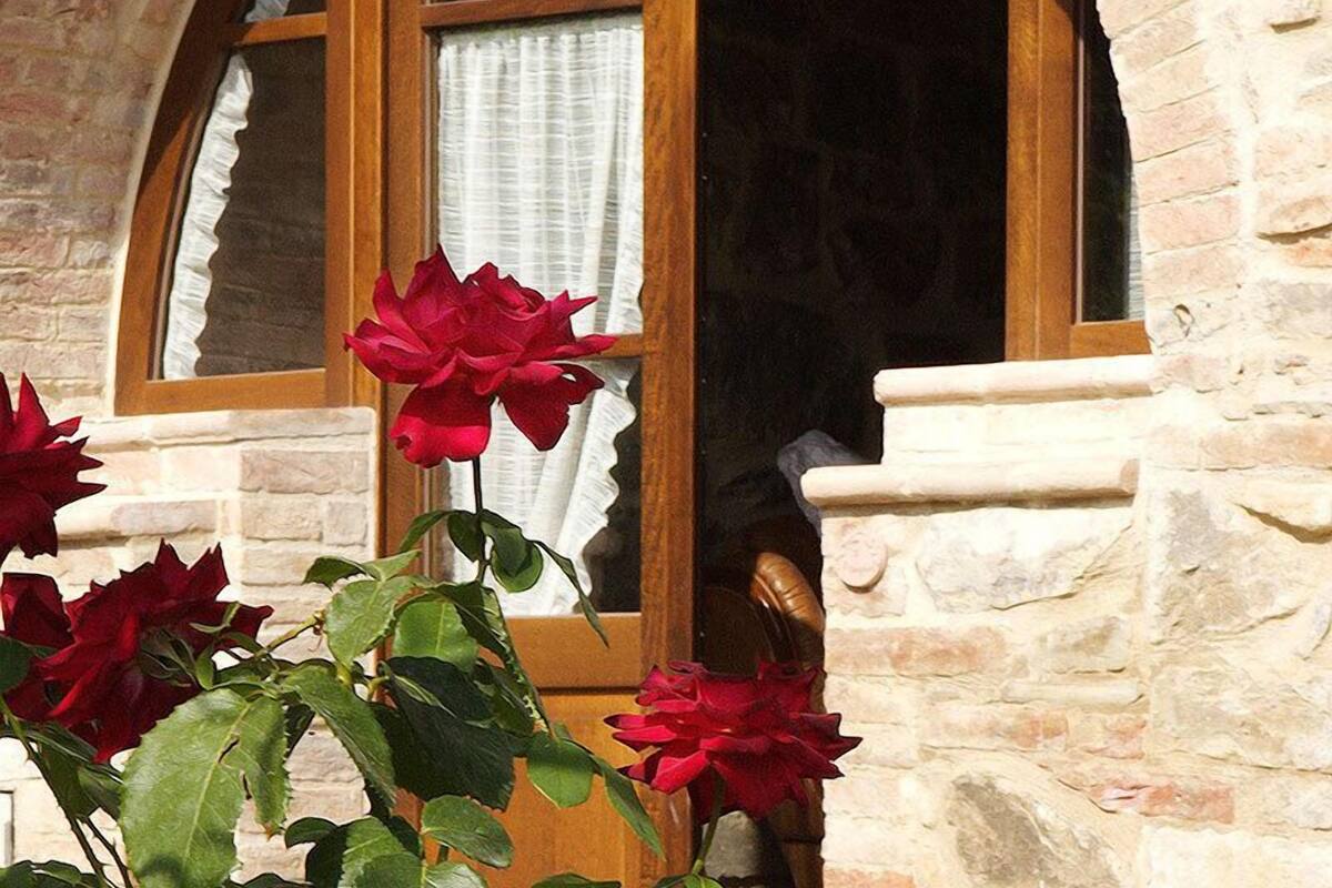 Ein Steinhaus mit einem Fenster und einem Rosenbusch im Vordergrund.
