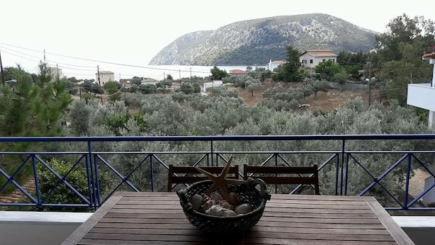 Mesa de madeira com um cesto contendo conchas e uma estrela-do-mar, com vista para uma paisagem montanhosa e um corpo d'água.