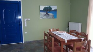 Uma área de refeições com mesa e cadeiras de madeira, um quadro na parede, uma porta azul e um radiador.