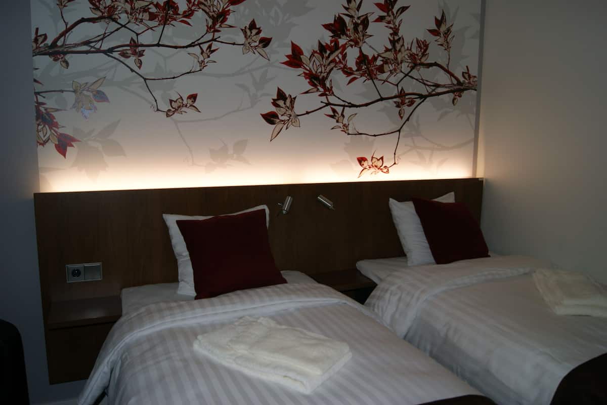 A hotel room with two beds, each with a red pillow and a white towel. The room has a wooden headboard and a wall with a floral mural.