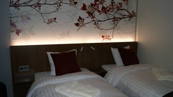 Een hotelkamer met twee bedden, elk met een rode kussens en een witte handdoek. De kamer heeft een houten hoofdbord en een muur met een bloemistisch schilderij.