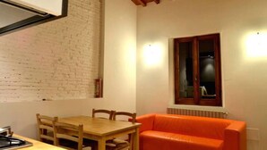 Una habitación con una mesa y sillas de madera, un sofá naranja, una pared de ladrillo y una ventana con radiador debajo.