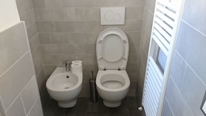 Un baño pequeño con dos inodoros, un bidé y un radiador.