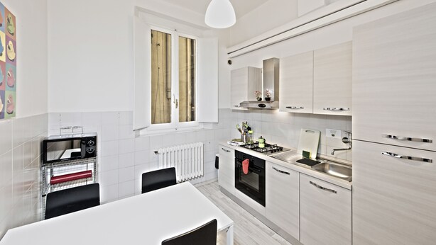 A modern kitchen with white cabinetry, a built-in oven, a microwave, and a window above the sink. - Santi Apostoli (Florence)
