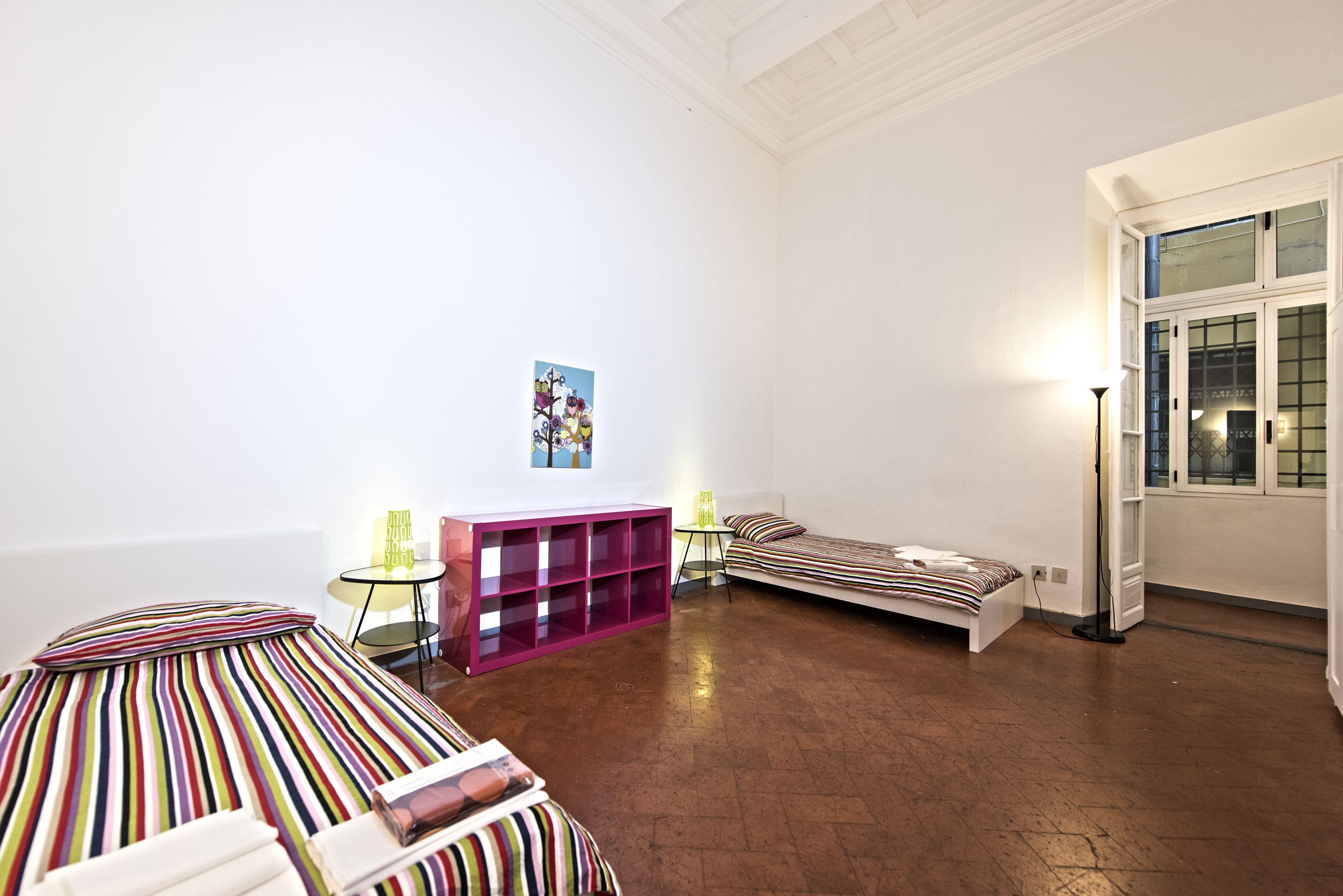 Une chambre avec un lit, une petite table, un meuble de rangement rose et une fenêtre donnant sur un beau paysage.