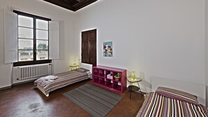 A room with two beds, a radiator, a window, a pink cabinet, and a small table. - Santi Apostoli (Florence)