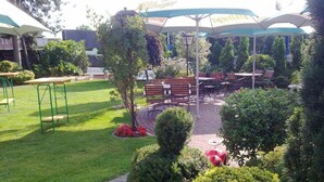 An outdoor patio area with tables and chairs under umbrellas, surrounded by greenery and a well-maintained lawn. - Hotel am Wintergarten (Bocholt)