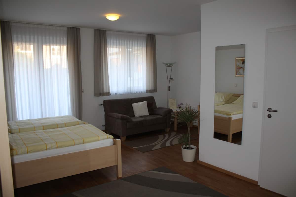 Ein Zimmer mit einem Bett, einem Sofa, einer Stehlampe und einem Blumentopf.