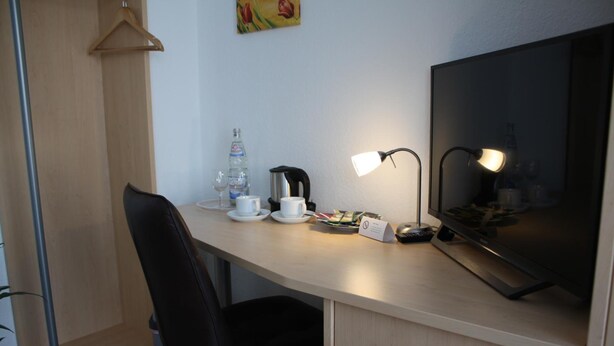 Habitación de hotel con escritorio, silla, televisor, cafetera, botella de agua y taza.