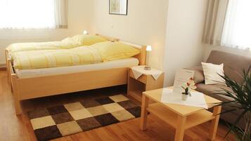 Habitación de hotel con cama doble, mesita de noche con lámpara, una pequeña mesa con menú, un sofá y un mostrador de recepción.