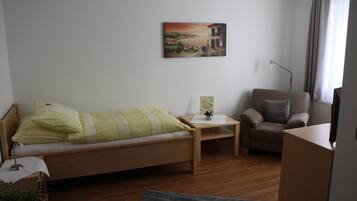 A bedroom with a bed, a chair, a small table, a lamp, and a painting on the wall.