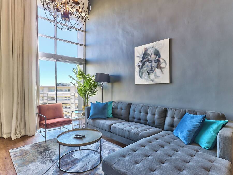 Una sala de estar moderna con un sofá seccional gris, una mesa de centro redonda y un ventanal con cortinas.