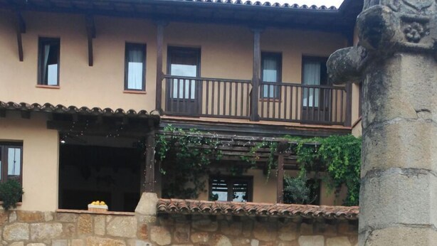 A courtyard with a stone building featuring a wooden door, potted plants, and a stone column. - La Picota (Valverde de la Vera)