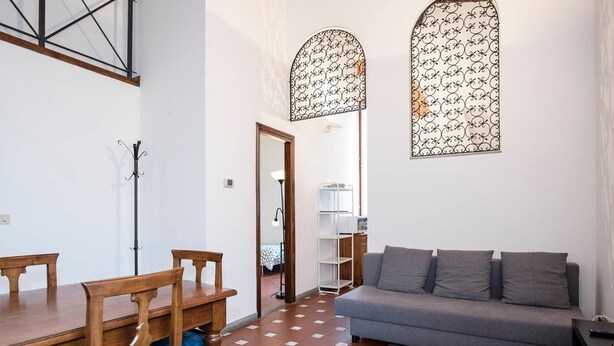 Una sala de estar con un sofá gris, una mesa de comedor de madera y sillas, y adornos decorativos en la pared con un estampado.