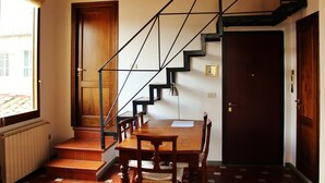 Una escalera con diseño geométrico, una mesa de comedor con sillas y vistas al exterior a través de una ventana.