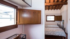 Un dormitorio con un armario de madera, una cama con ropa de cama estampada y una ventana que da a vistas de edificios.