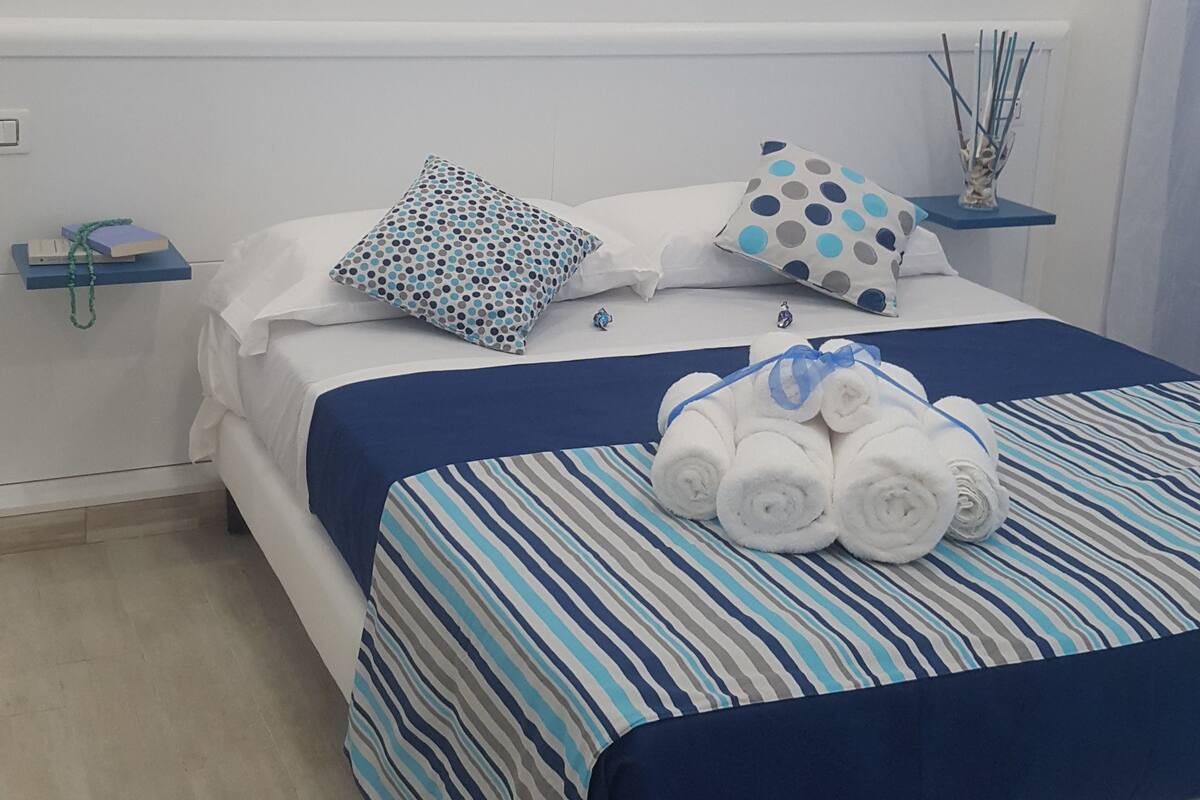 Un dormitorio con cama, almohadas, un adhesivo mural de pájaros y una mesita de noche con un florero.