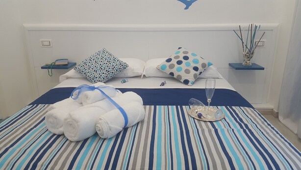 Una cama bien tendida con ropa de cama a rayas, dos almohadas con estampado de lunares, un vaso de agua y una bandeja con un adorno.