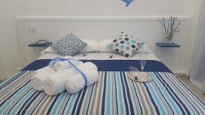A neatly made bed with striped bedding, two pillows with polka dot patterns, a glass of water, and a tray with a decorative item. - Residenza Burmaria (Tropea)
