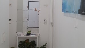 Un pasillo con una puerta blanca, un banco con plantas y un espejo instalado en la pared.