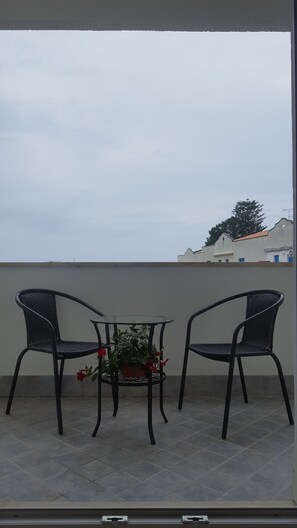 A balcony with two wicker chairs and a small table with a potted plant.