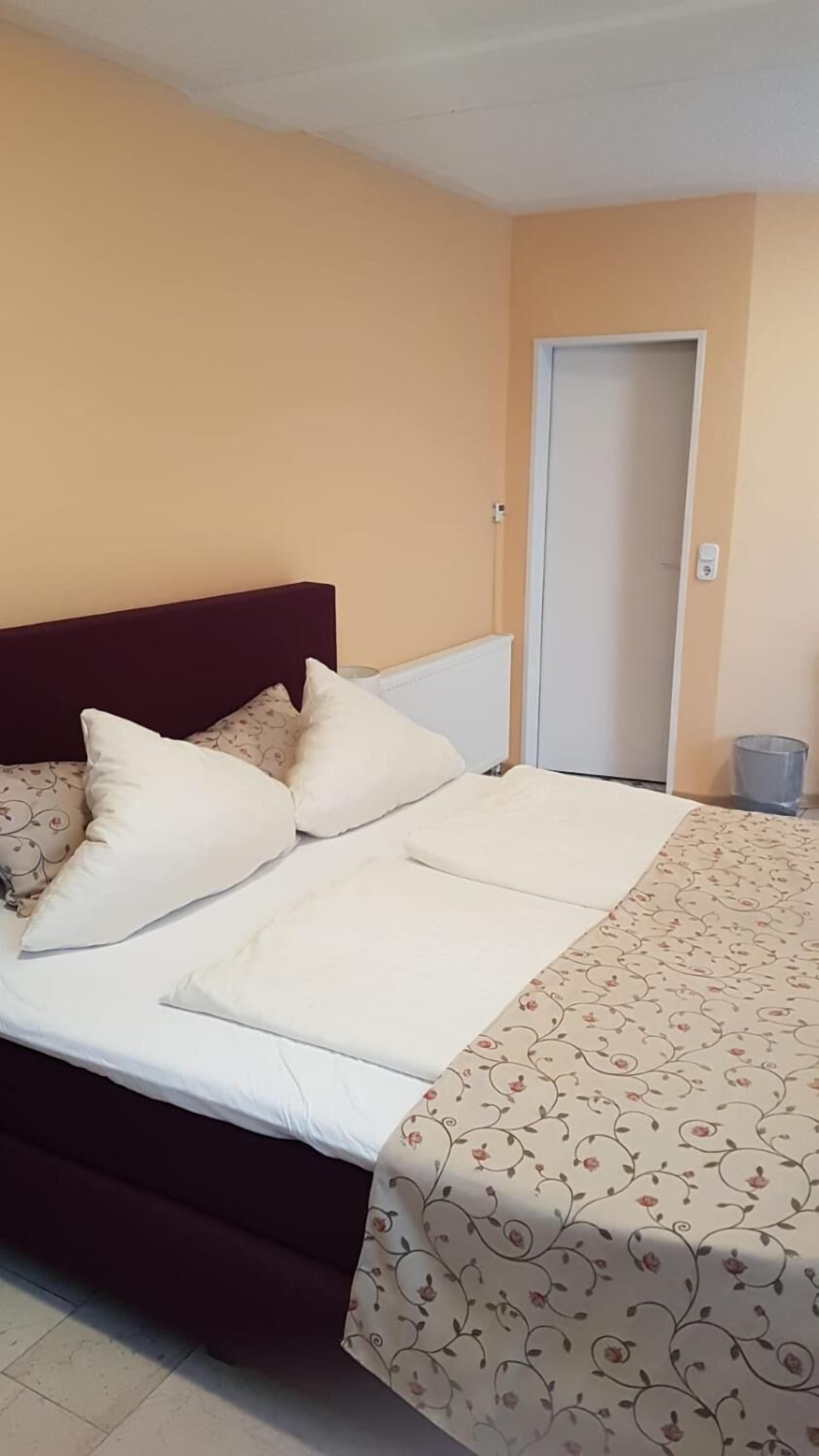 A bed with white linens and a floral-patterned duvet, a dark headboard, and a door in the background.
