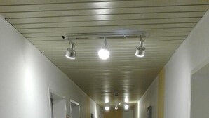 A long, narrow hallway with white walls and a tiled floor. There are several doors on the left side, and the ceiling has recessed lighting. - Hotel Hafez (Bad Salzuflen)