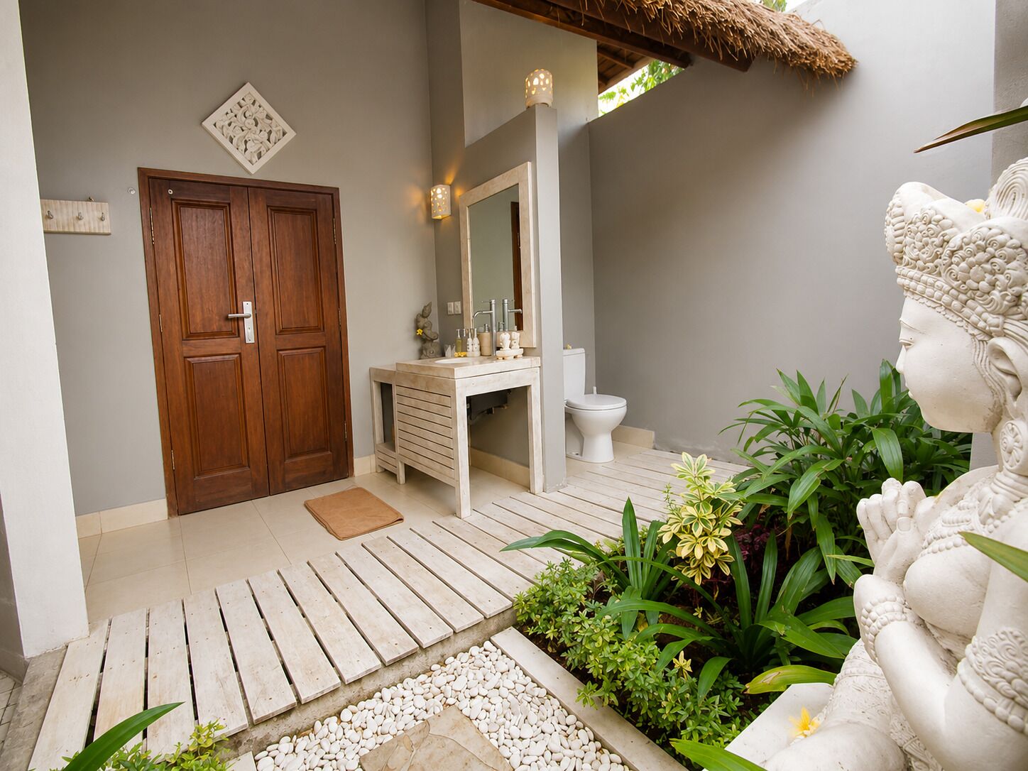 Een badkamer met een houten deur, een witte wasbak, een spiegel en een toilet.