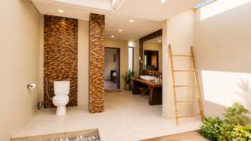 Une salle de bain moderne avec des toilettes, un lavabo et un espace douche. On y trouve une échelle en bois et un petit coin jardin agrémenté de galets et de plantes.