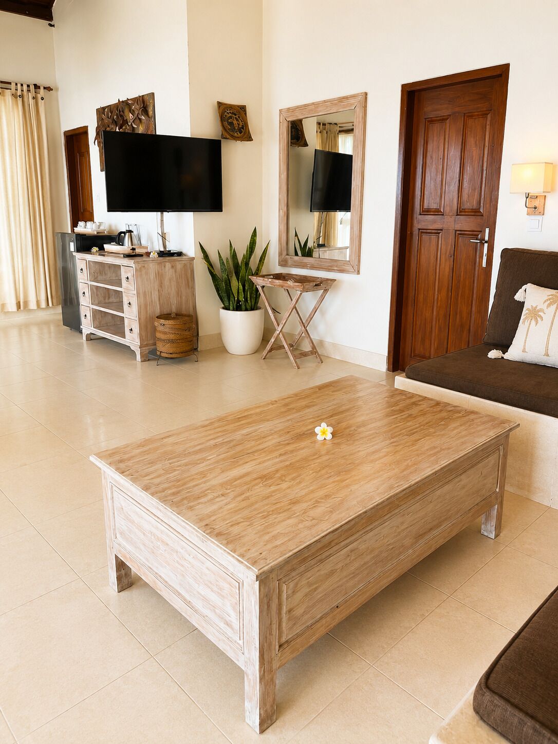 Una sala de estar con una mesa de centro de madera, un televisor de pantalla plana, una planta en maceta, un mueble de madera y un sofá marrón.