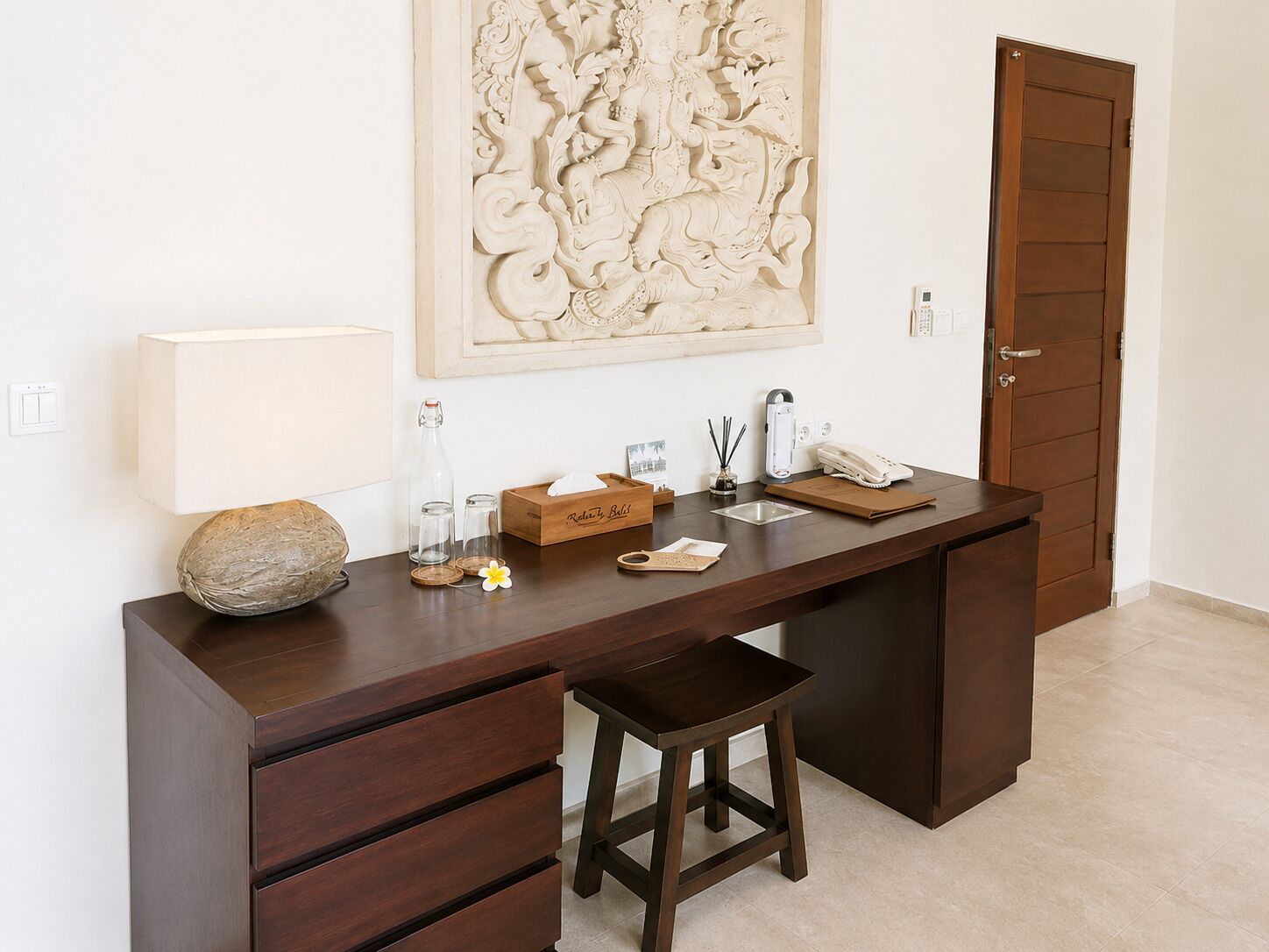 A modern office desk with a lamp, a decorative vase, a telephone, and a small stool.