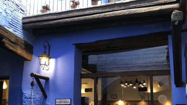 Un edificio con fachada azul, un letrero que dice "CAFETERIA" y un pozo de piedra.