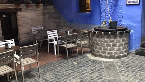 Un café con mesas al aire libre, suelo de piedra y pared azul.