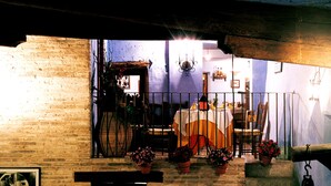 Un área de comedor al aire libre con pared de ladrillo, plantas en macetas y una mesa preparada para dos personas.