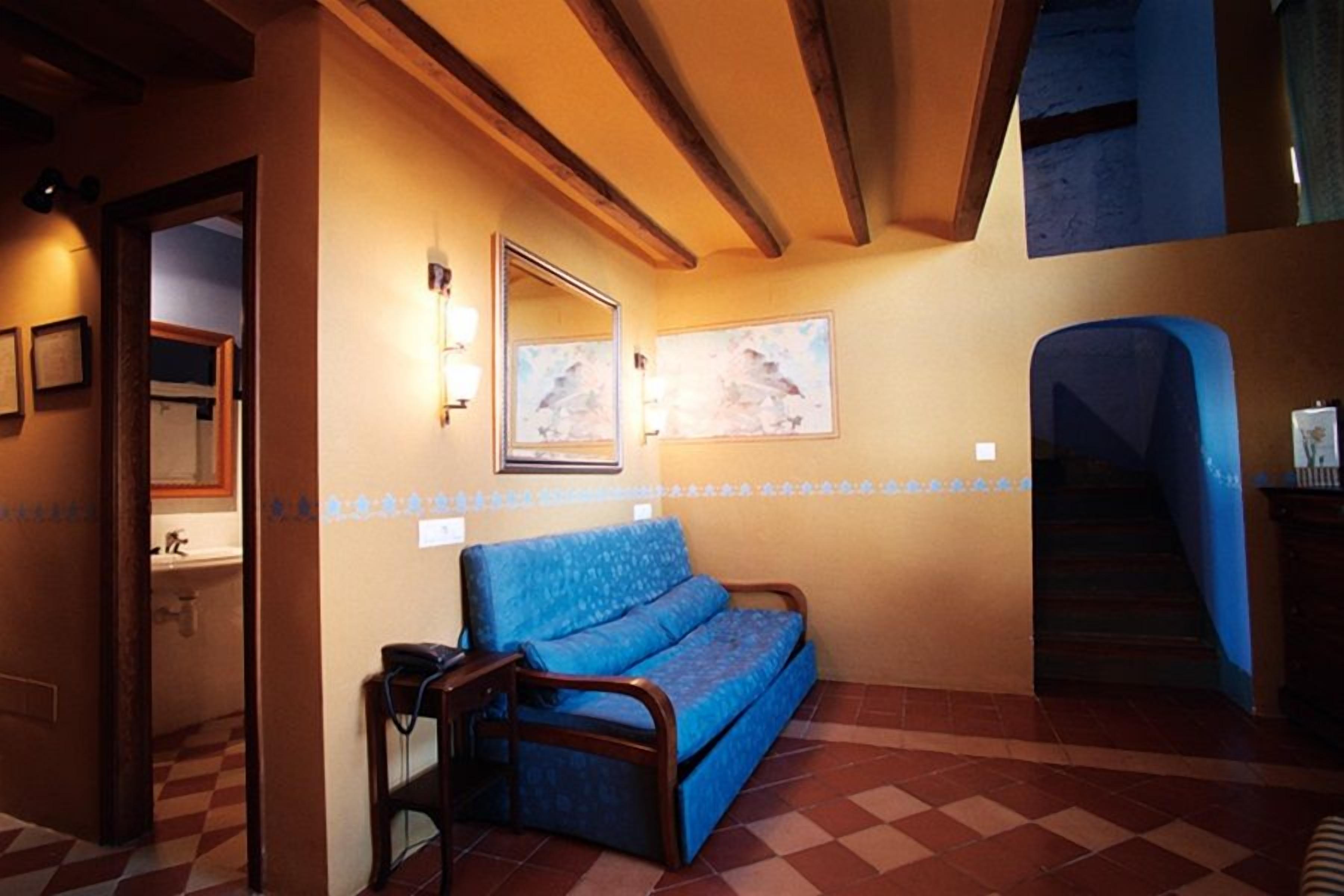 Una habitación con un sofá azul, una silla de madera, un espejo fijado en la pared y una escalera.