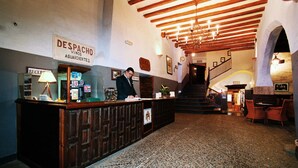 Un área de recepción con un escritorio de madera, un letrero que dice "DESPACHO VINOS AGUARDIENTES" y una escalera que sube a los pisos superiores.