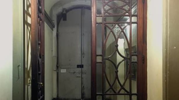 A hallway with a checkered floor leading to a door with a decorative metal gate. - Spadolini Apartment (Florence)