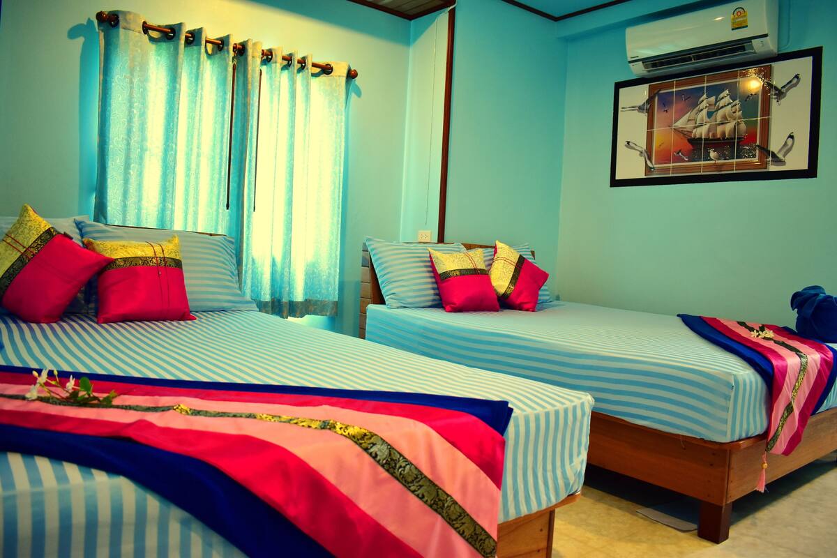 A room with two beds, each with striped bedding and pillows, a window with curtains, and a framed picture on the wall.