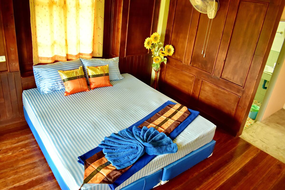 A neatly made bed with striped bedding, a blue and brown checkered blanket, and a blue towel.