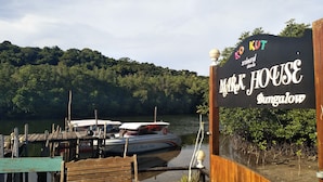 Un muelle de madera con un letrero que dice 'Mr. K House Bungalow' y un barco llamado 'J.J. Boat Trip' atracado cerca.