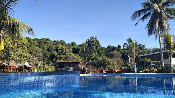 Una piscina azul cristalina rodeada de palmeras y un pequeño edificio con la leyenda 'TOILET'.