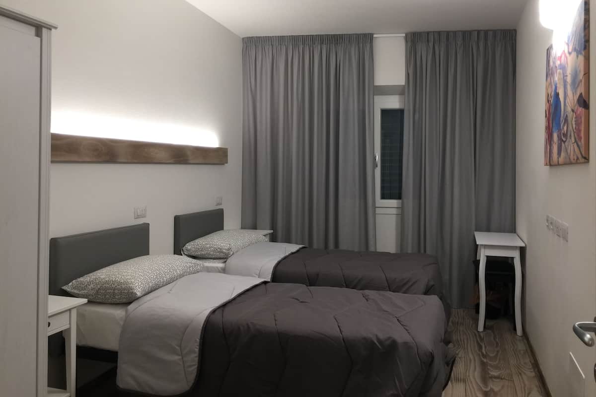 Habitación de hotel con dos camas, un escritorio pequeño, una ventana con cortinas y un cuadro en la pared.