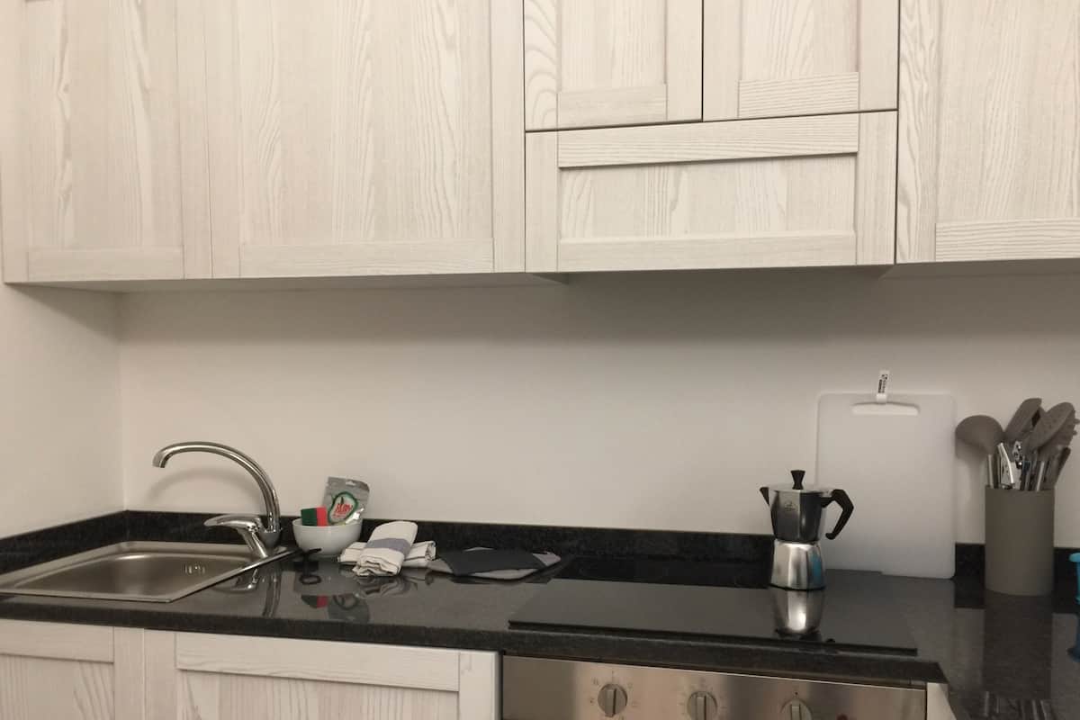 Una cocina con armarios blancos, un lavamanos de acero inoxidable, una estufa y una cafetera.